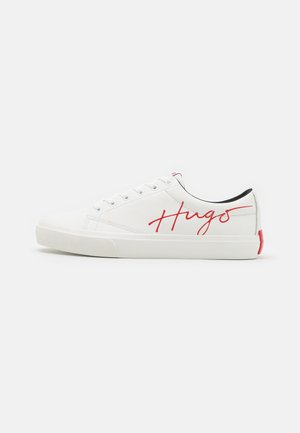 White low-top sneaker with white laces, red "Hugo" script on side, black inner lining, and a red pull tab on the heel.