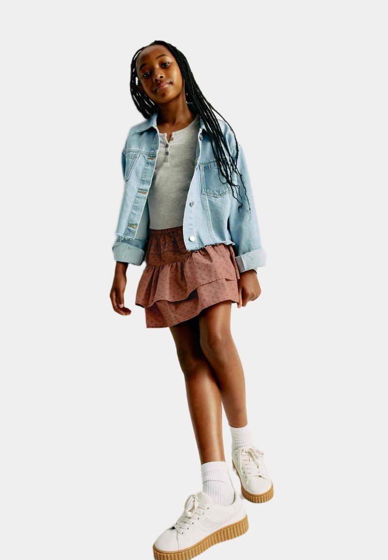 Jeansjacka, grå kortärmad skjorta, volangkjol i brunt med prickar, och vita sneakers med en texturerad sula.