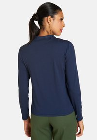 Navyblaues Langarmshirt aus weichem Stoff, mit schlichtem Design und geradem Saum. Kombiniert mit grünen Hosen, die einen lockeren Sitz zeigen.