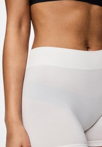 Baltās augstas jostasvietas leggingas, kas izgatavotas no gludas, elastīgas auduma. Tiem ir ribota josta un puscaurspīdīgs apdare.