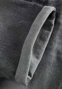 Mörkgrå denimtyg som visar en veckad kant med en ljusare grå innerfoder, med en subtil ribbad textur och sömdetaljer.