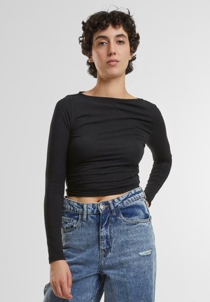Zwarte langarm crop top met een bootlijnhals, aansluitend ontwerp en een gladde textuur, gecombineerd met hoog-waist lichtblauwe jeans met verachte details.