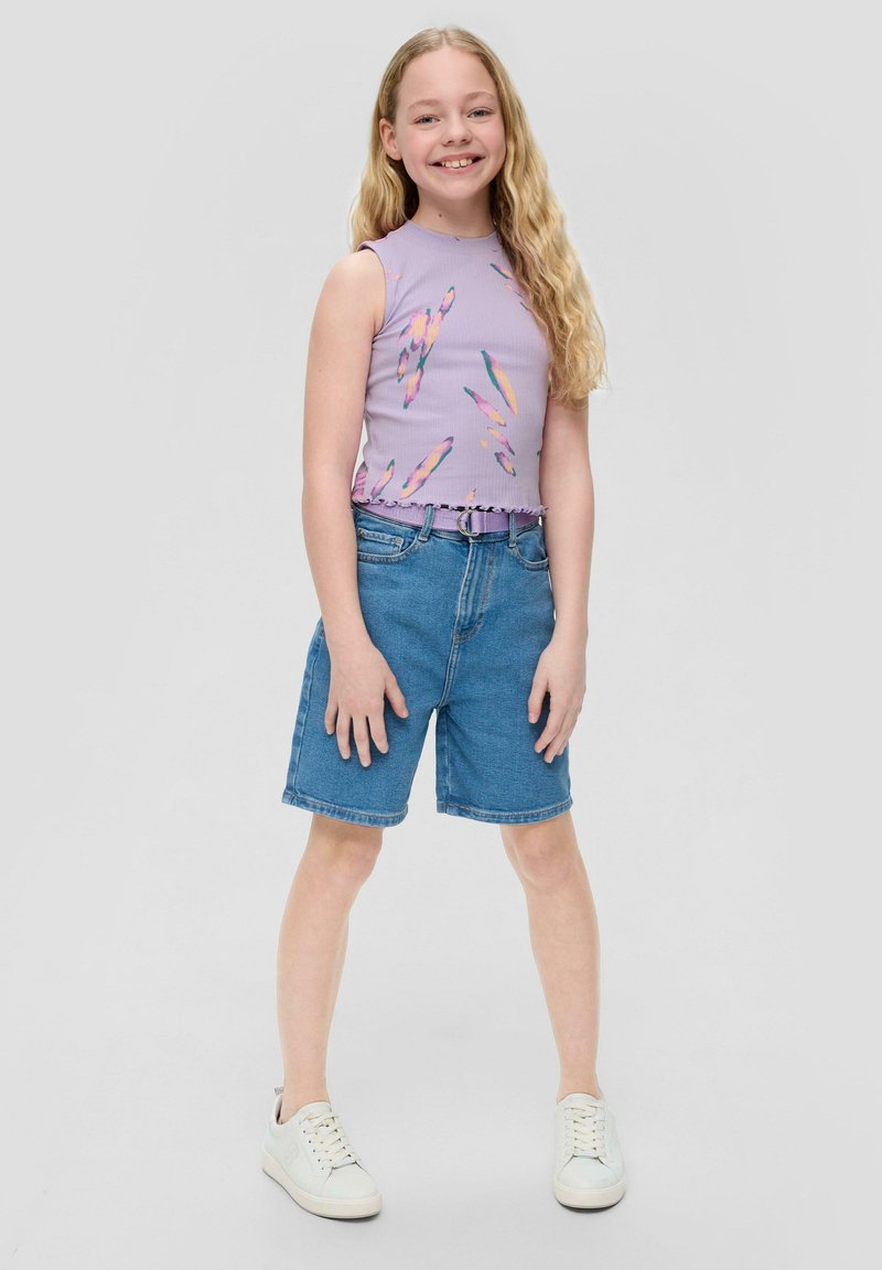 Top viola senza maniche con un motivo multicolore, abbinato a pantaloncini di denim blu e scarpe da ginnastica bianche. Visibile l'orlo arricciato del top.