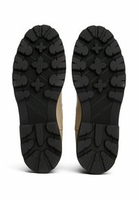Suela de zapato de goma negra con un patrón de relieve texturizado que presenta formas circulares y en cruz, acompañada de una parte superior en tono marrón.