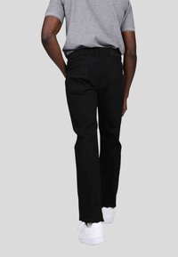 Jeans en denim noir avec une coupe droite, dotés de poches arrière et d'une ceinture épurée, associés à des baskets blanches et un t-shirt gris.