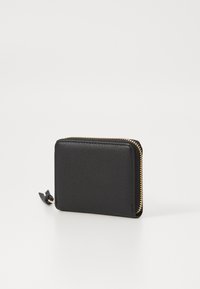 Cartera de cuero negro con superficie texturizada, forma cuadrada, zipper dorado y una pequeña lengüeta de cuero. Diseño minimalista.