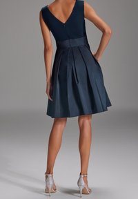 Granatowa sukienka z V-kształtnym tyłem, rozkloszowanym fasonem i plisowanym dołem. Połączona z srebrnymi szpilkami dla dodatkowego kontrastu.