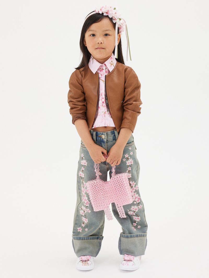 Giacca bomber marrone, camicia floreale rosa, jeans in denim ricamati con fiori rosa, borsa a tracolla di perline rosa, sneakers bianche con dettagli floreali.