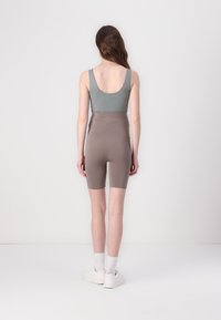 Bodysuit senza maniche grigio chiaro con schiena bassa, abbinato a pantaloni bike beige a vita alta. Texture liscia, design minimale e lunghezza fino al ginocchio.