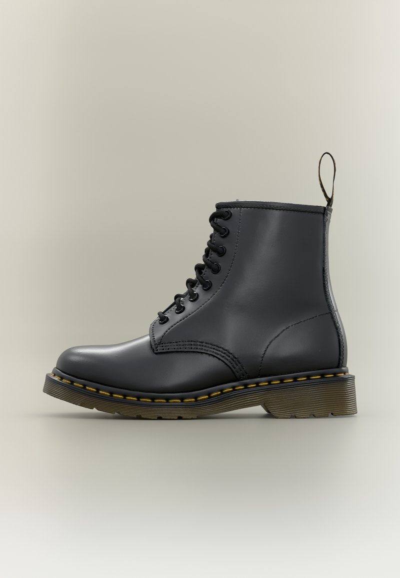 Bottine noire en cuir à lacets avec surpiqûres jaunes, semelle rainurée et languette à l'arrière sur fond neutre.