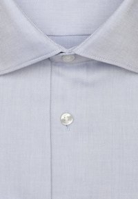 Chemise à rayures bleu clair avec un col classique et une fermeture à un bouton au cou, réalisée dans un tissu tissé lisse.