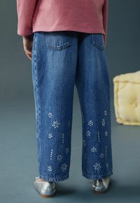 Pantaloni evazați din denim albastru închis, cu broderii florale argintii pe partea inferioară a picioarelor. Au buzunare la spate și un croi lejer.