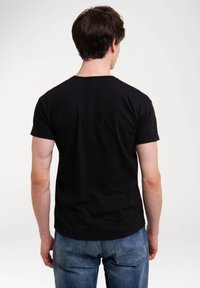 Schwarzes Baumwoll-T-Shirt mit Rundhalsausschnitt, kurzen Ärmeln und taillierter Passform, kombiniert mit blauen Jeans. Glatte Textur ohne sichtbare Muster.