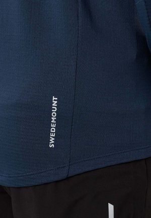 Primo piano di tessuto blu navy con testo verticale "SWEDMOUNT" in bianco e tessuto nero con un piccolo disegno bianco in basso.