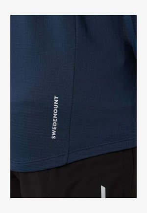 Primo piano di tessuto blu navy con testo verticale "SWEDMOUNT" in bianco e tessuto nero con un piccolo disegno bianco in basso.