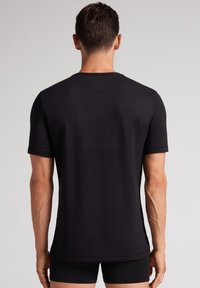 Camiseta negra de manga corta con cuello redondo, hecha de tela suave, con un corte recto y detalles de costura mínimos.