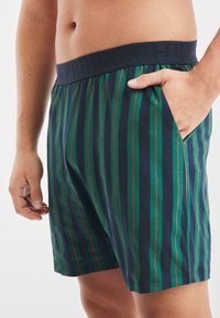 Bomullboxershorts med vertikala ränder i marinblått, grönt och rött. Elastisk midjeband med präglad text; sidficka på höger sida.