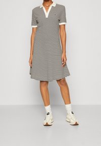 Pruhované šaty s bílým límcem a krátkými rukávy, vyrobené z měkké tkaniny. Sukně se jemně rozšiřuje a má střídající se černé a bílé pruhy.