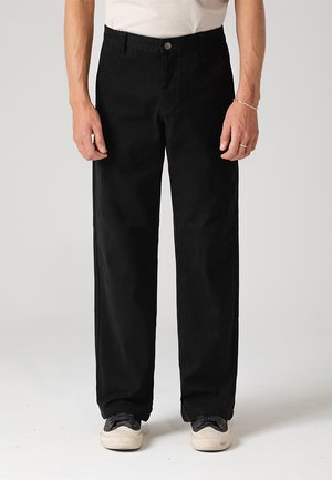 Fekete pamut nadrág, egyenes szárú fazonban, elülső gombos zárással és oldalsó zsebekkel, fekete športcipővel párosítva.