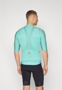 Kurzarm-Radtrikot in Mintgrün mit atmungsaktiven Netzeinsätzen, figurnaher Passform und Rückentaschen. Schwarze gepolsterte Shorts ergänzen das Outfit.