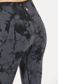 Leggings en tie-dye noir et gris avec une taille haute, dotées d'un tissu texturé et d'un petit logo circulaire près de la taille.