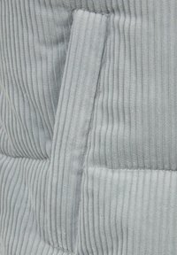 Close-up van lichtgrijze geribbelde stof met een verticale band en zichtbare stiksel details.