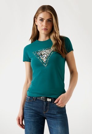 Tricou scurt, de culoare teal, cu un grafic în formă de triunghi cu imprimeu de leopard și detalii metalice. Asortat cu blugi din denim albastru.