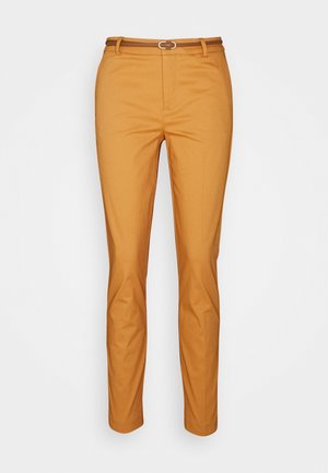 Pantalones ajustados de color mostaza con un cinturón fino marrón y un cierre frontal oculto sobre un fondo blanco.