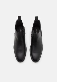 Bottes cheville en cuir noir à finition lisse, avec des panneaux élastiques latéraux et une languette pour faciliter l'enfilage. Design minimaliste avec une forme pointue à l'avant.