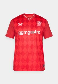 Červený futbalový dres s diamantovým vzorom, krátke rukávy, V-výstrih a bielym logom. Na prednej strane sú uvedené názov značky a sponzor.