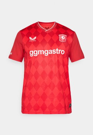 Red soccer jersey with diamond pattern, short sleeves, a V-neck, and white logo. Features brand name and sponsor on the front.
