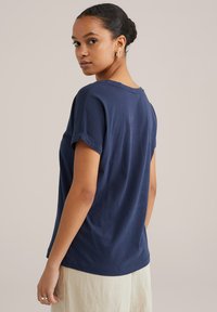 Kleita jūras zilā krāsā ar īsām piedurknēm, izgatavota no mīkstas kokvilnas, ar apaļu kakla izgriezumu un sarullētām piedurknēm. Aizmugurē ir vienkāršs, neuzkrītošs dizains.