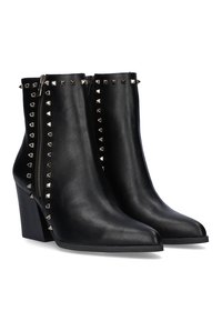 Botas de tobillo de cuero negro con punta afilada, que presentan tachuelas metálicas a lo largo de la cremallera y el costado, y un diseño de tacón grueso.