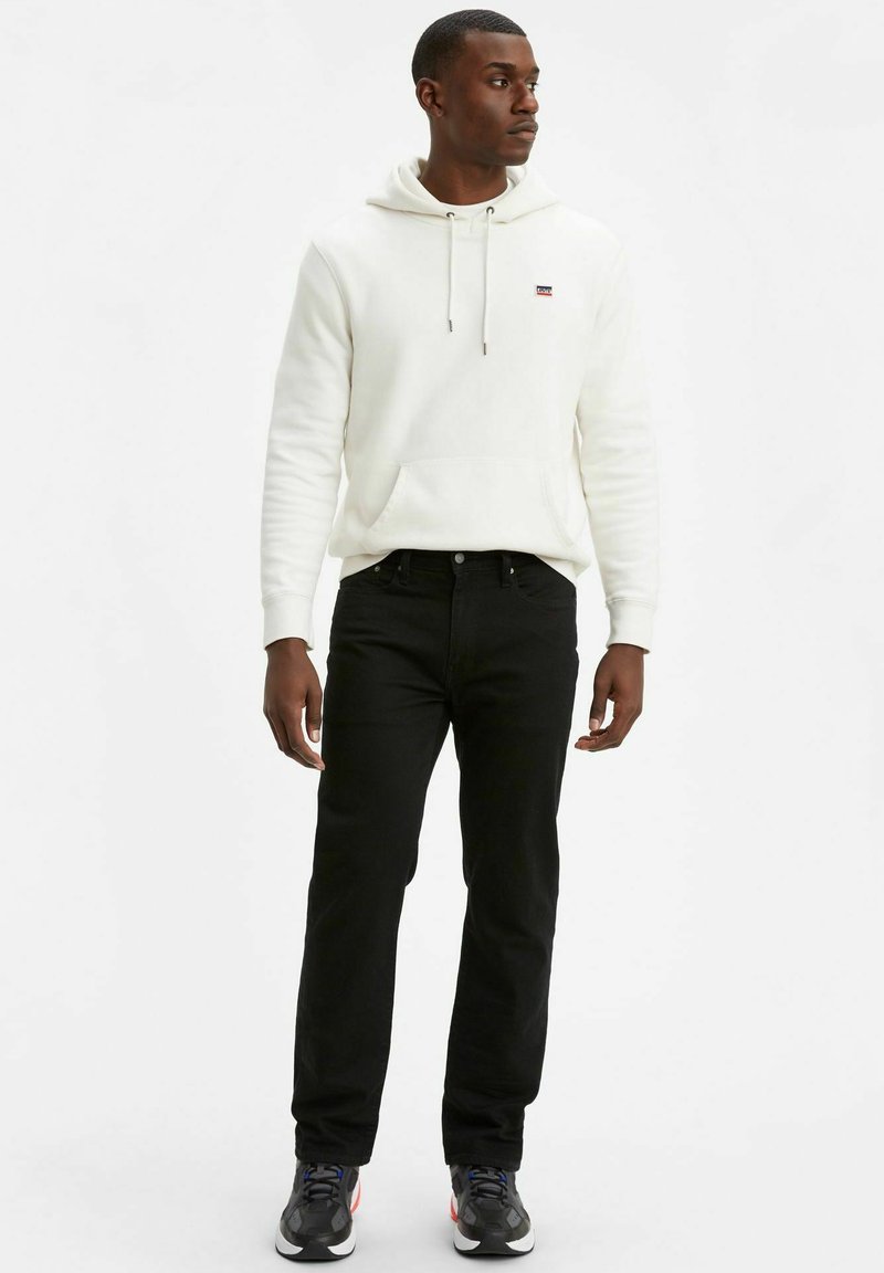 Vit hoodie med en framficka och snörning, ihop med svarta jeans och svarta sneakers med färgdetaljer. En enkel och avslappnad outfit.