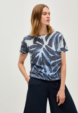 Blaue und weiße kurzärmlige T-Shirt mit einem Palmenblattmuster auf einem strukturierten Stoff, kombiniert mit lockeren dunkelblauen Hosen.