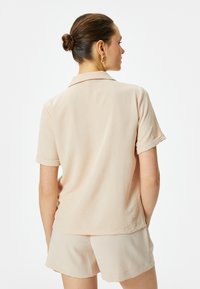 Korte mouwen, overhemd met kraag in lichtbeige gestructureerde stof, gecombineerd met bijpassende beige shorts, gepresenteerd vanuit de achterkant.