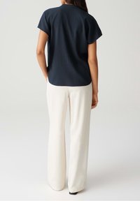 Haut texturé bleu marine à manches courtes, ourlet arrondi, associé à un pantalon large crème clair et des chaussures noires, vu de dos.