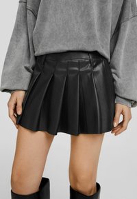 Schwarzer plissierter Lederrock mit tailliertem Bund, glatter Textur und ausgestelltem Saum, kombiniert mit einem grauen, übergroßen Sweatshirt.