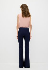 Marinblå utsvängda byxor med bakfickor, i kombination med en ljusrosa ärmlös topp. Slät tygtextur, åtsittande midjeband och minimalistisk design.