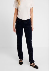 Tummansininen corduroy-housut slim fit -mallissa, varustettu nappikiinnityksellä, etutaskuilla ja hienovaraisella brändikorostuksella vyötäröllä.