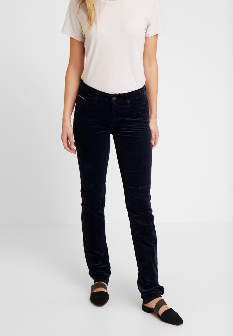 Tummansininen corduroy-housut slim fit -mallissa, varustettu nappikiinnityksellä, etutaskuilla ja hienovaraisella brändikorostuksella vyötäröllä.