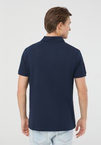 Granatowa koszulka polo z klasycznym kołnierzykiem i krótkimi rękawami, wykonana z gładkiego materiału, prezentowana z tyłu, z delikatną teksturą.