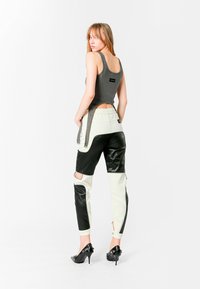 Top ajustado gris sin mangas con tirantes, combinado con pantalones en dos tonos que presentan cuero negro y cuero sintético color crema, y zapatos de tacón alto negros.
