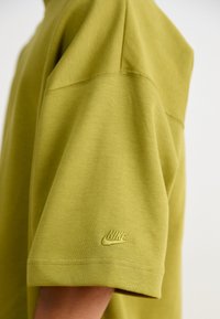 Zaļa īsām piedurknēm T-kreklu, kas izgatavots no mīksta auduma, ar apaļu kakla izgriezumu un mazu, izšūtu Nike logo kreisajā piedurknē.