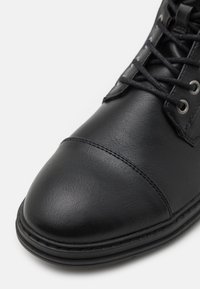 Bota de cuero negro con punta redonda, parte superior texturizada y ojales para los cordones. Incluye costuras contrastantes alrededor de la suela.