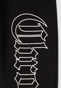 Czarna tkanina z dużym białym tekstem graficznym o ostrych kątach i zarysowanych detalach, podkreślająca odważny, graficzny design.