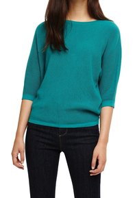 Miętowy sweter z prążkowanego materiału, z rękawami o długości trzech czwartych i szerokim dekoltem, zestawiony z ciemnymi dżinsami. Tekstura jest miękka i lekka.