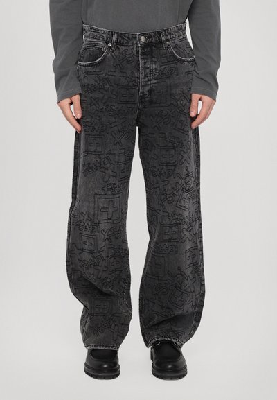 Pantaloni in denim neri con un motivo a rilievo su tutta la superficie, vestibilità ampia, cinque tasche e cuciture a contrasto. Abbinati a calzature nere.