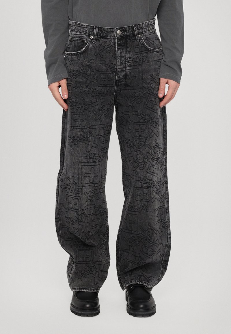 Pantaloni din denim negri cu un model embosat pe toată suprafața, croială largă, cinci buzunare și cusături contrastante. Asortați cu încălțăminte neagră.