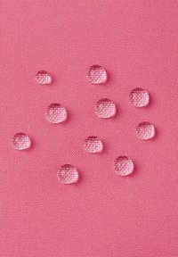 Wodoodporna różowa tkanina z wyraźnymi kroplami tworzącymi się na jej teksturowanej powierzchni, ukazująca gładkie, lekko błyszczące wykończenie.